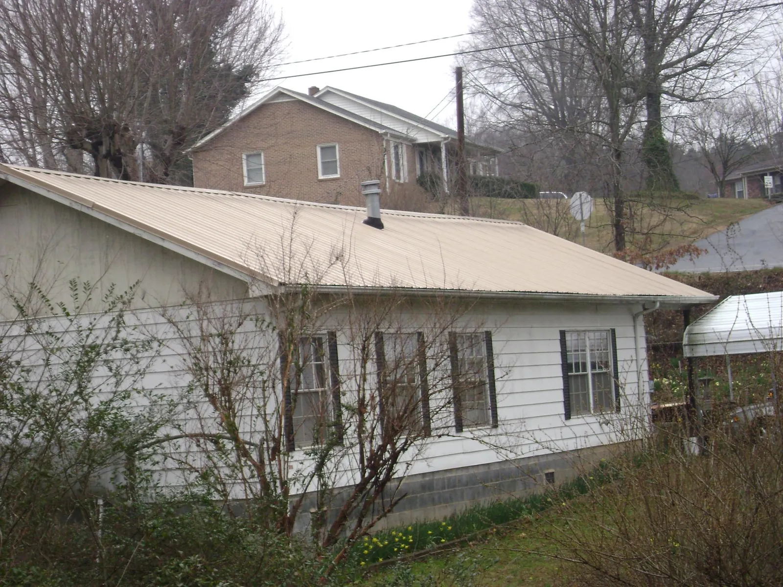 Tan metal roof on a white sided house set into a hillside — Commercial Roofing by Roofing Brothers in Dover